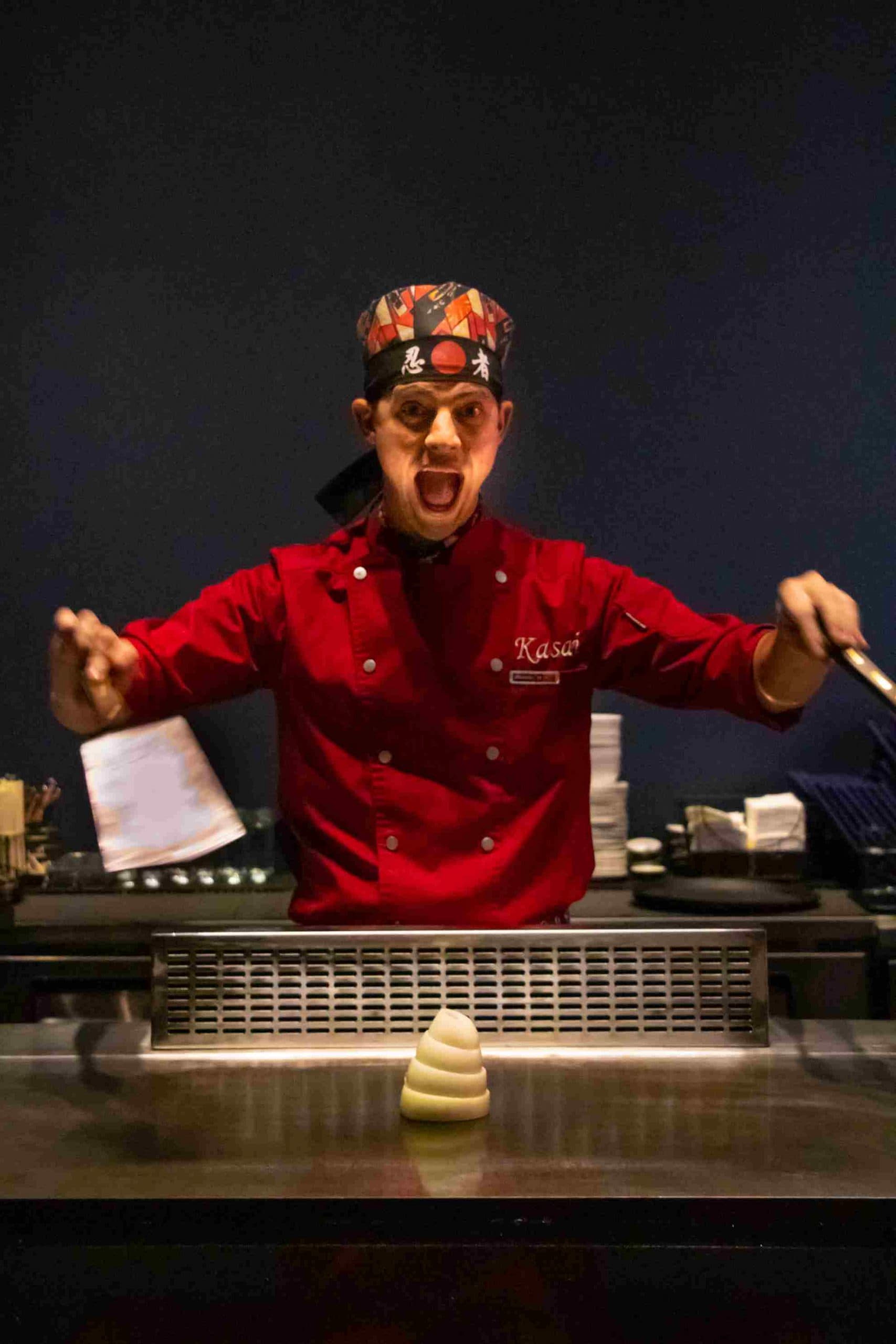 A Kasai chef mid-performance, arms wide behind the teppanyaki grill