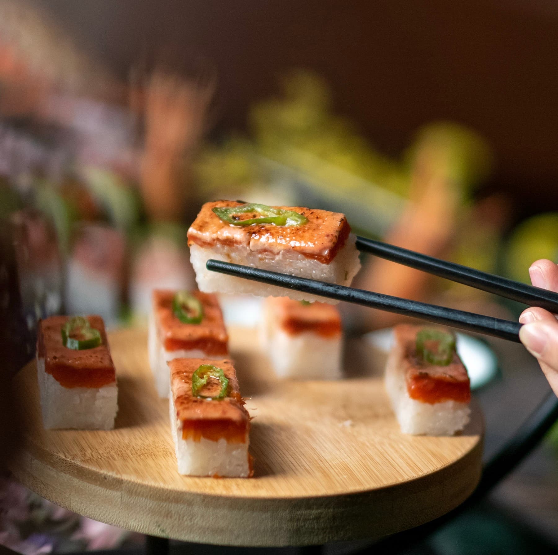Aburi oshi sushi on a wooden board, one piece lifted with chopsticks