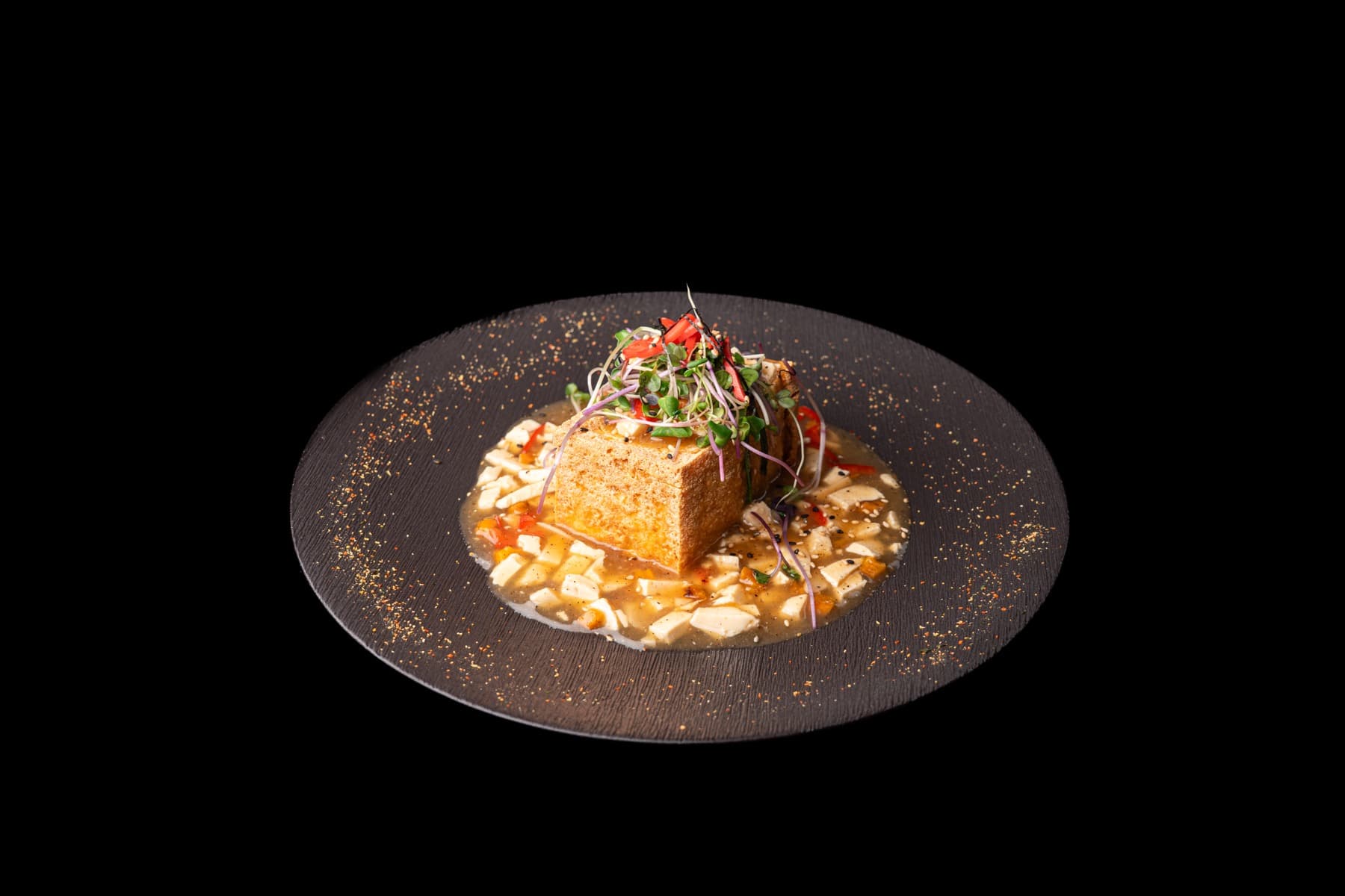 Lava tofu with microgreens and chilli, plated on a round black dish