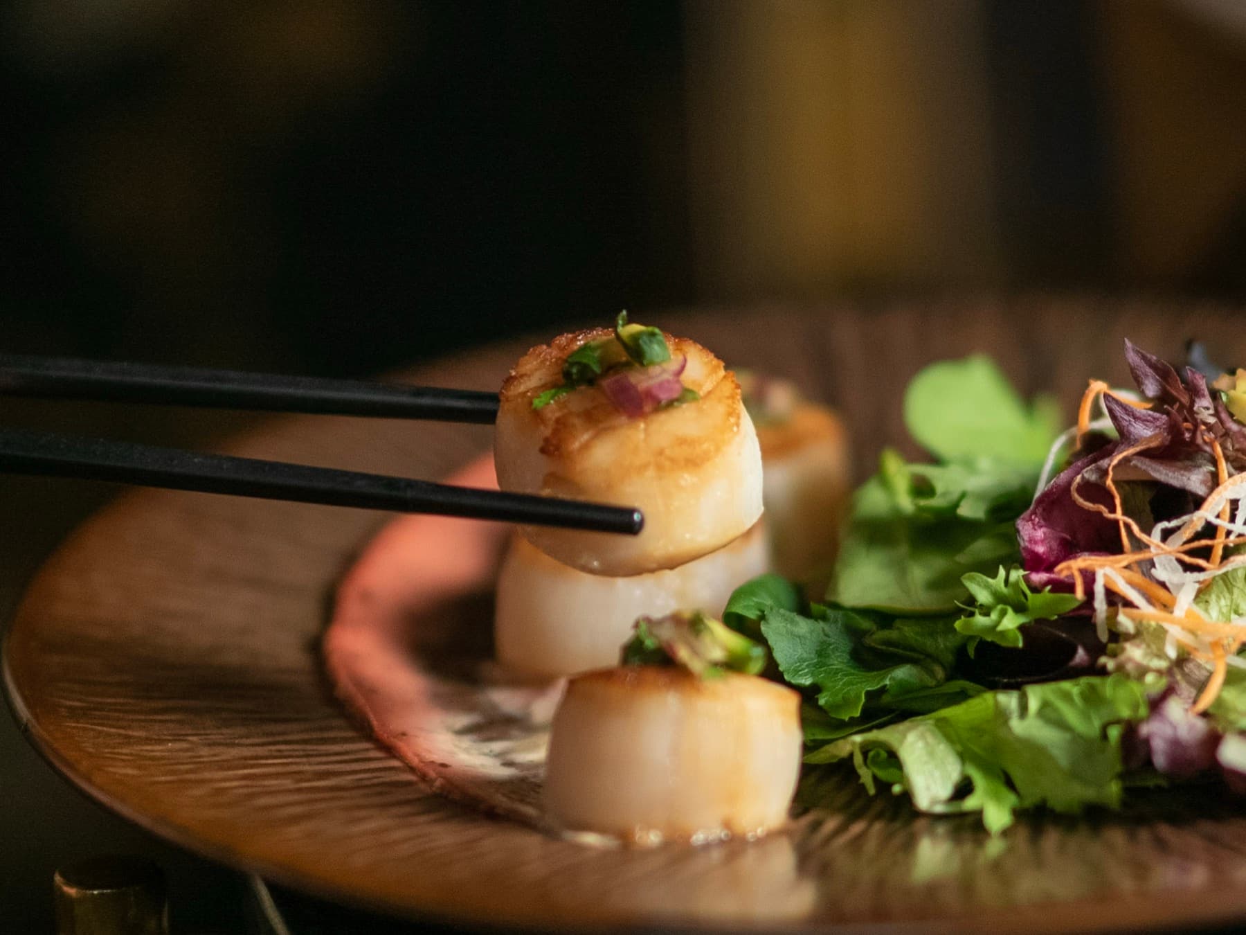 Ume grilled scallops with spring mix, served on a dark plate