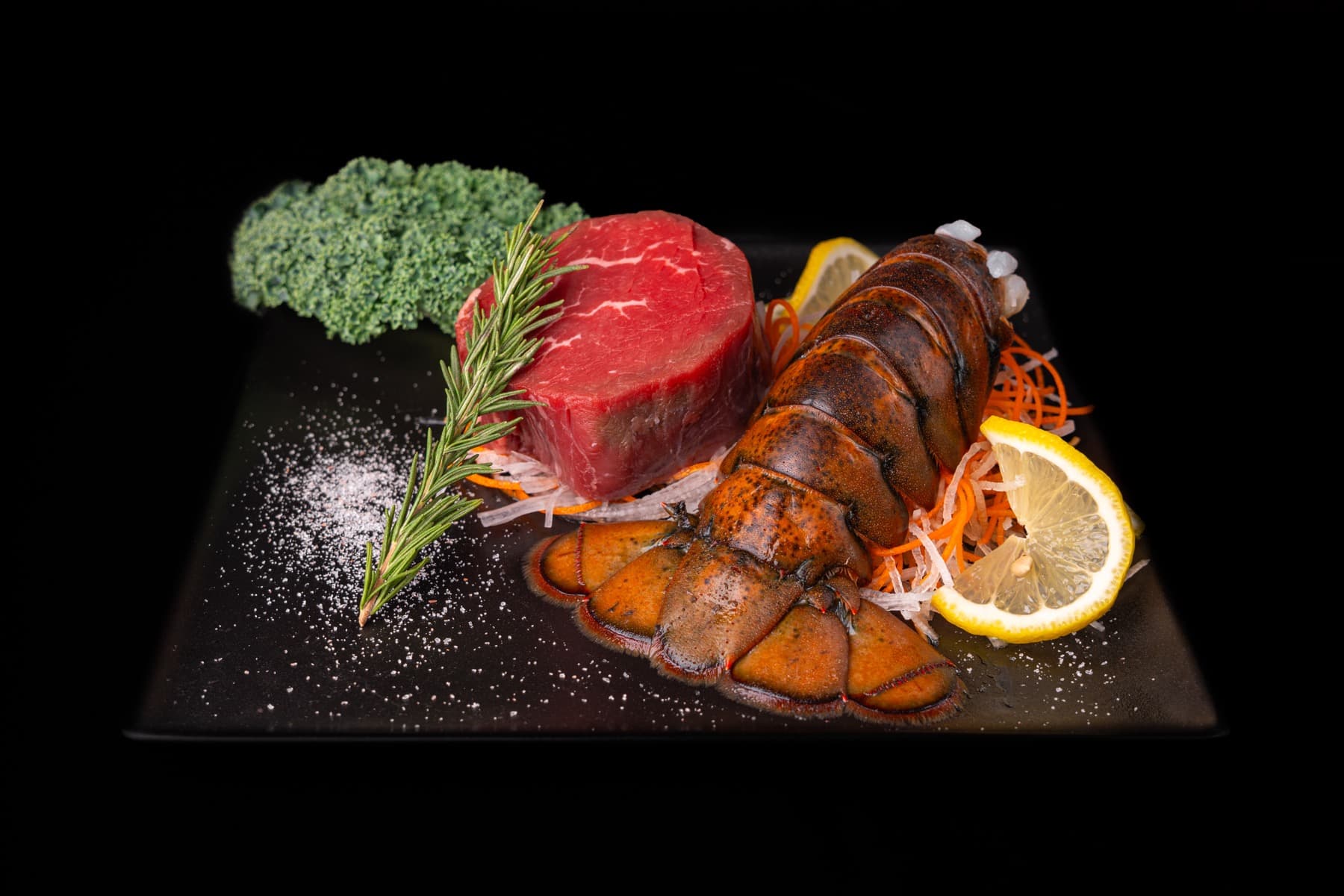 Filet mignon and a whole lobster tail plated on slate with rosemary and lemon
