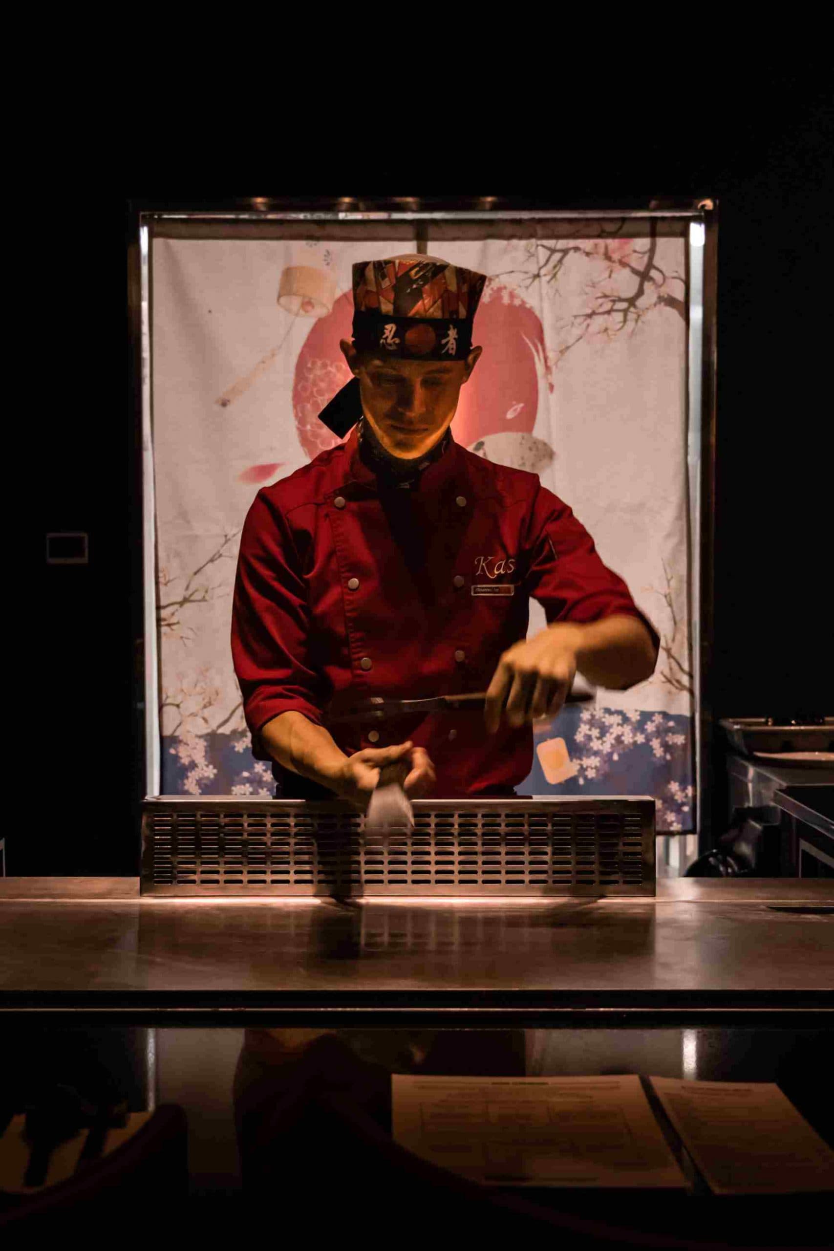 A Kasai chef working the griddle in front of a cherry-blossom noren curtain