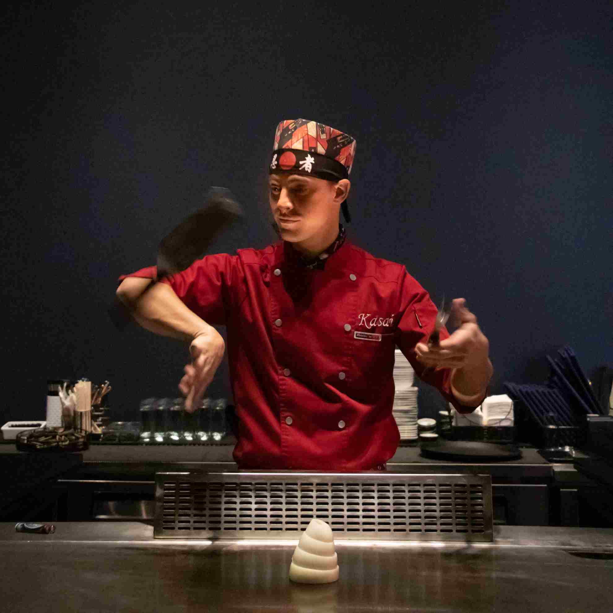 A Kasai chef mid-performance, flipping utensils above the teppanyaki grill