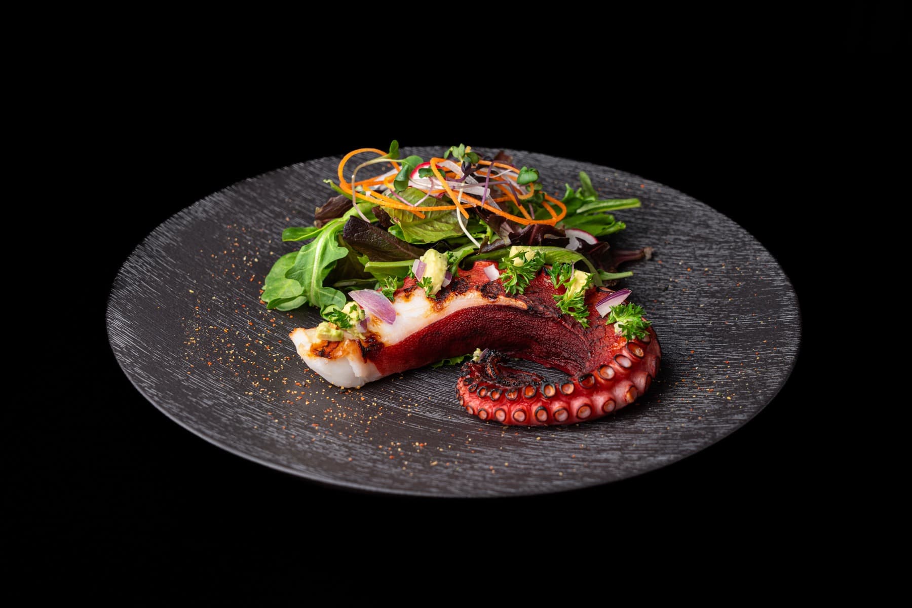 Grilled octopus with spring mix on a dark stone plate
